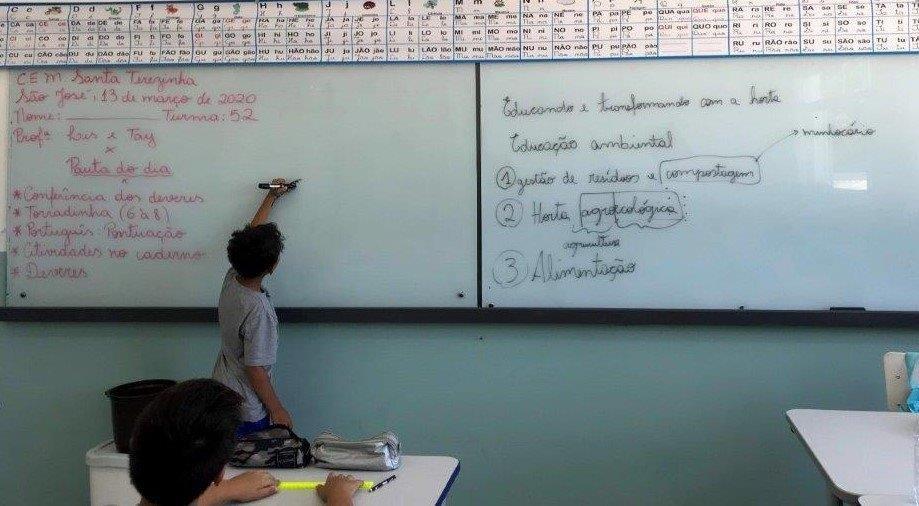 menino escrevendo no quadro branco em frente a sala de aula