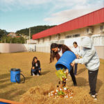 Um menino e uma menina jogam os resíduos da bombona azul na composteira.