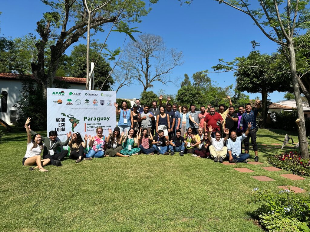 Foto do Comitê Gestor do projeto "Agroecologia na América Latina: construindo caminhos" reunido ao lado de uma painel com o nome do projeto e as logos das organizações participantes.